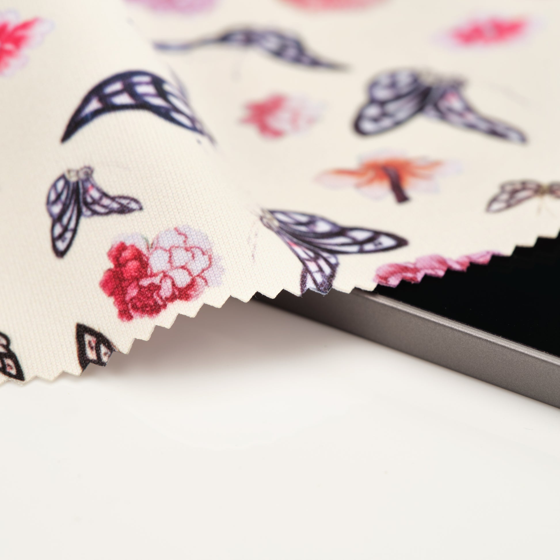 A close up of the lens cloth showing detail of the design and high quality edging. The cloth design features butterflies and pink flowers on a light background. 