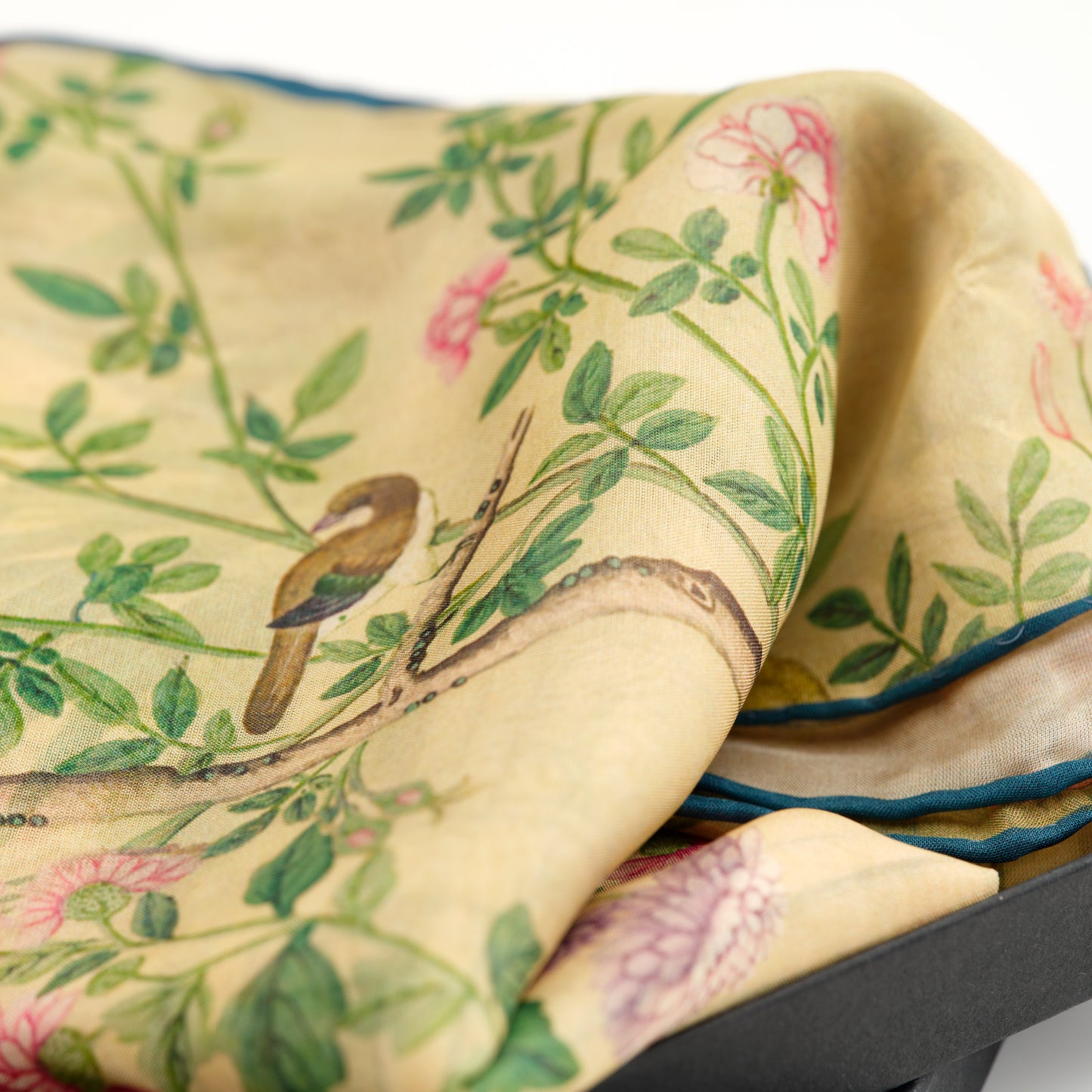 A close up look at a pastel yellow chiffon scarf decorated with birds, flowers and tree branches.