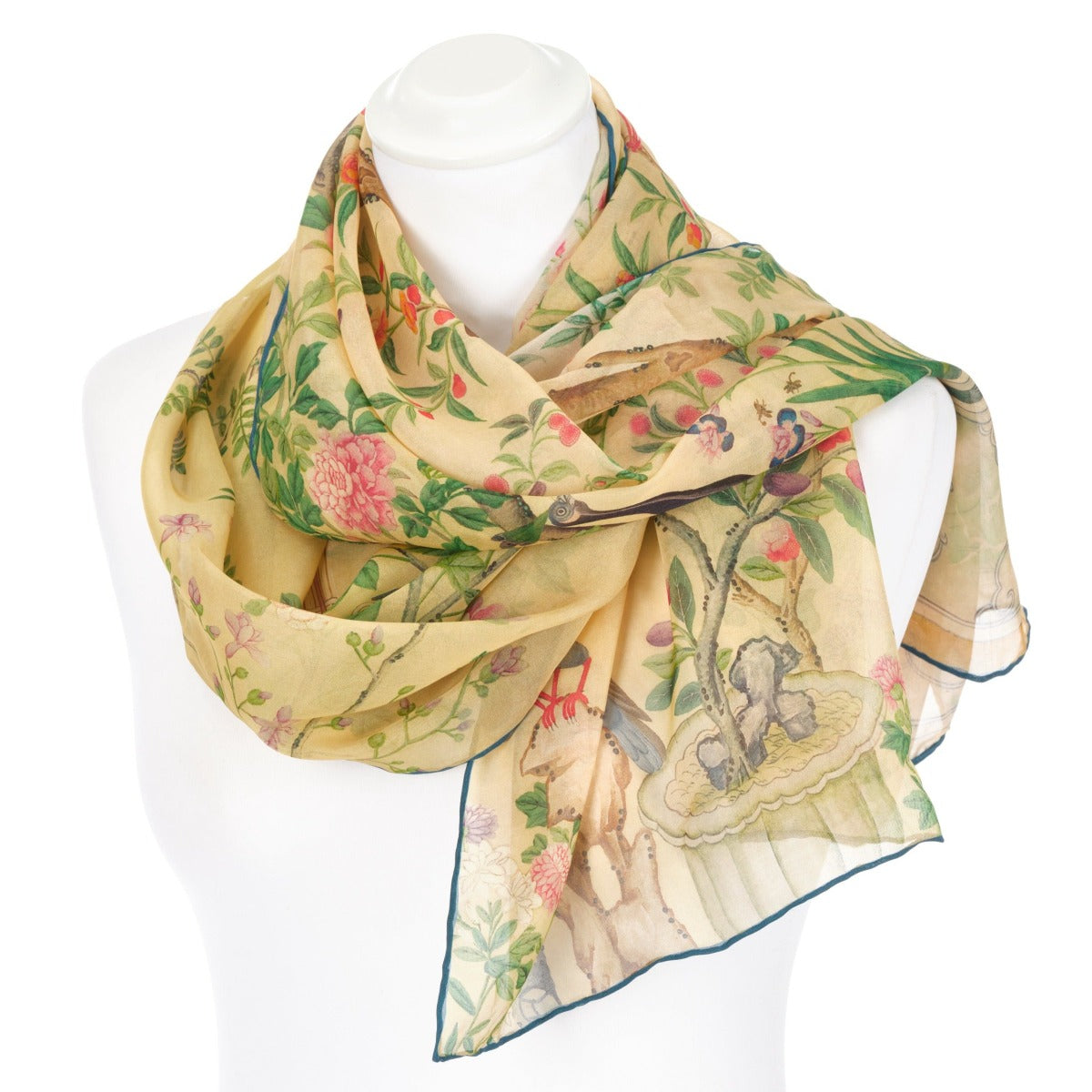 A pastel yellow chiffon scarf draped over a mannequin on a white background. The scarf design features birds, flowers and tree branches.