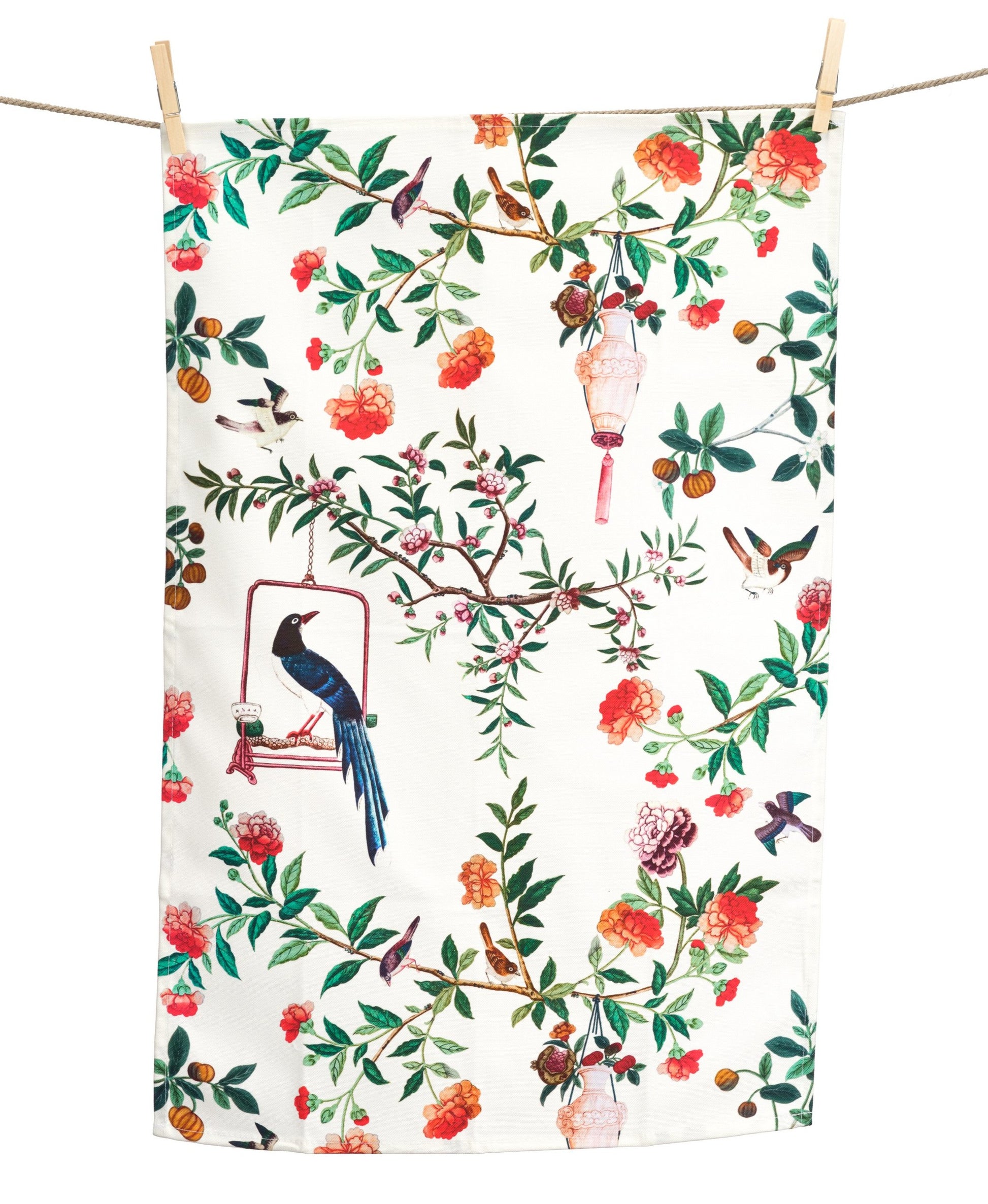 A tea towel hanging from a washing line. The design features a bird perched on a swing and lanterns hanging from tree branches.